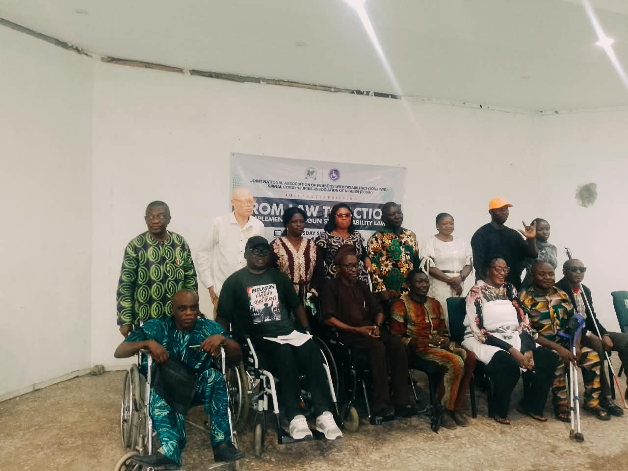 Ogun PWD Groups Demand Implementation of Disability Law Nine Years After Assent Group photograph of persons with disabilities and disability advocates gathered at a press briefing on the implementation of the Ogun State Disability Law. Several participants are seated in wheelchairs or using mobility aids, while others stand behind them. A banner in the background reads “From Law to Action: Implement the Ogun State Disability Law.”